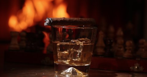 Glass of whiskey with smoking cigar.Glass of alcohol and smoking noble cigar on  the background of flames in the fireplace 
