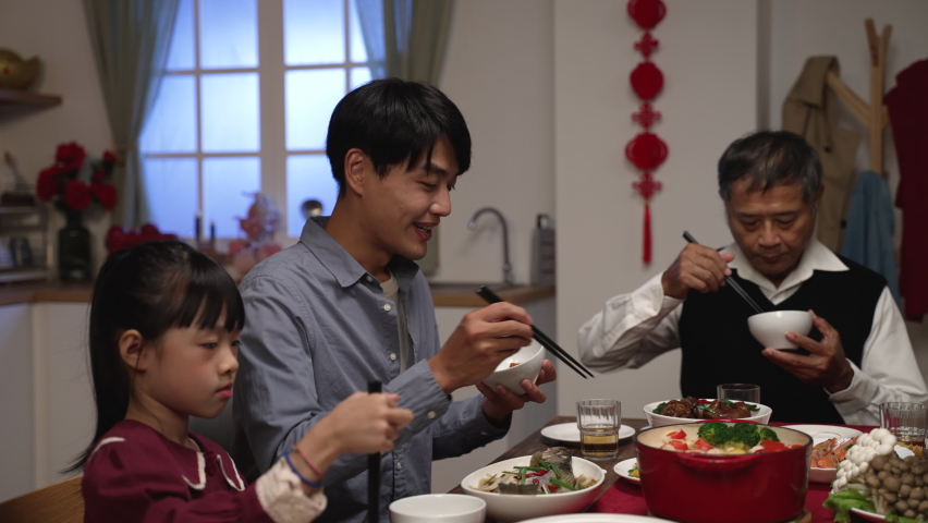 happy chinese father talking to his daughter while enjoying big meal with family. mixed generation having chinese lunar new year dinner at home. Royalty-Free Stock Footage #1083612610