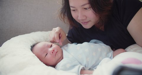 Portrait happiness Asian mother playing with her pretty newborn baby infant girl lying on bed in the morning at home, children, parenthood, childhood, life, maternity, motherhood concept