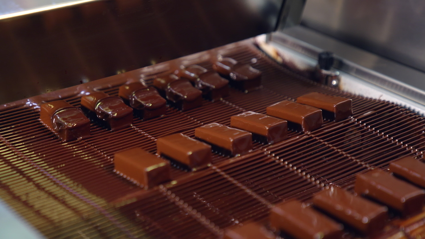 Pouring chocolate at a candy factory for the production of chocolates. Sweets are poured with chocolate on production line at a candy factory close up. Royalty-Free Stock Footage #1083618130