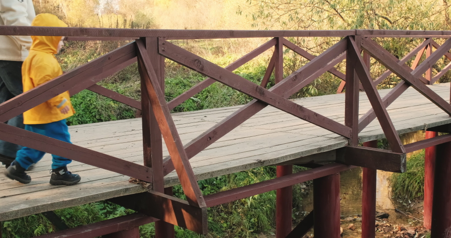 Small child walking with his mother in autumn forest. Family walks across wooden bridge over a stream. The concept of childhood, happy family and lifestyle. Nature, clean air, active rest on weekends
