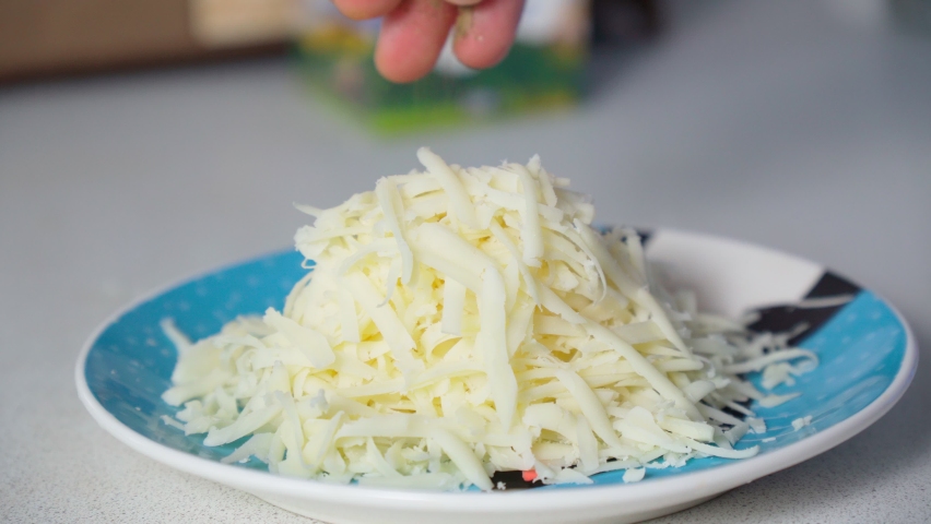 Adding basil spice to grated cheese close-up. Cooking