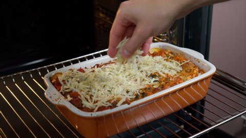 Baking Lasagne Bolognese in Electric Oven, adding cheese. Selective focus