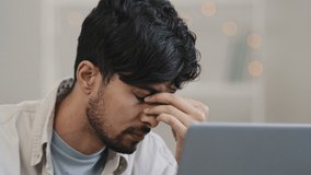 Close-up male focused arabic young guy business man freelancer looking at laptop tired discomfort in eyes pain worrying problem bad news takes off glasses holding bridge of nose headache exhaustion - Powered by Shutterstock - Get 15% off with code: PIKWIZARD15