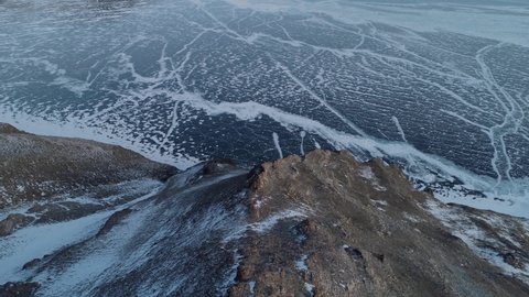 Aerial epic winter frozen lake Baikal cracked ice endless field, open space. Snowy cliffs mountains amazing nature landscape. Siberia Russia costal north scenery. Travel tourism. Fast forward motion