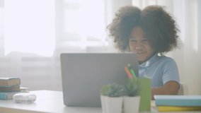 Happy little black girl having video call on computer, talking to tutor online