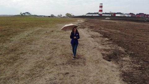 A girl in a blue cardigan and jeans is dancing with an umbrella against the background of the lighthouse