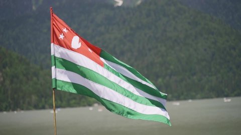 The state flag of the country of Abkhazia against the background of the beautiful Lake Ritsa