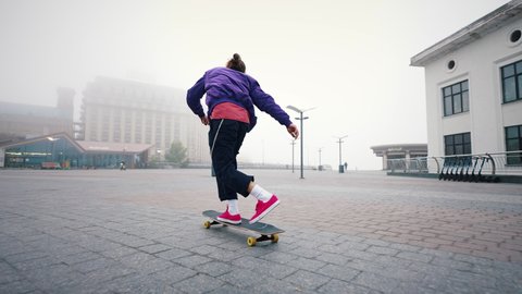 Rear view of young modern guy training his skateboarding skills in an empty city square on a foggy autumn morning outdoors. Find your freedom. ஸ்டாக் வீடியோ