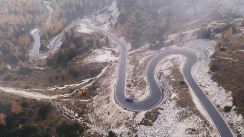 Aerial drone view on winding mountains road leading to Three peaks of Lavaredo in Tre Cime di Lavaredo National Park in Dolomite Alps. Foggy larches forest around. Autumn in Dolomites, Italy