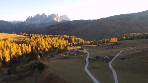 Drone flyght over Fuchiade valley in Italian Dolomites countryside in autumn time. Wooden huts, orange larches forest and mountains peaks on background. Dolomite Alps, Italy. UHD 4k video