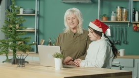 Grandmother and Granddaughter Celebrate Christmas or New Year Online Using a Video Call on A Laptop. Virtual Family Holiday Online Chat, Fun Communication, Celebration, Generational Communication.