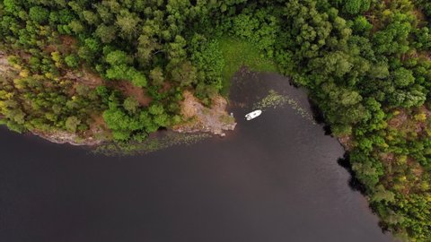 Boat anchored at quiet place of calm Murolahti bay, top-down aerial shot. Camera slowly move down. Swampy area seen near with rocky shore, trees grow at stony hills of Ladoga skerries