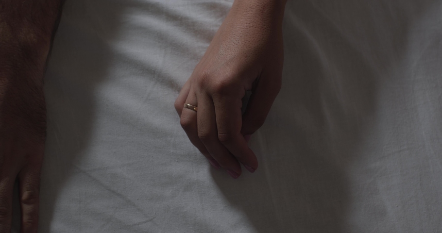 Close-up woman and man hand in hand on a white bed sheet. Couple reconciles, reunites after breaking up, or supports each other in difficult situation. Relative on duty in patient
