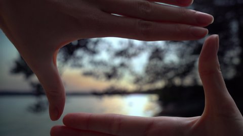 Finger Frame. Woman folding her hands in frame with sunset on a Midsummer night on a forest lake in Finland