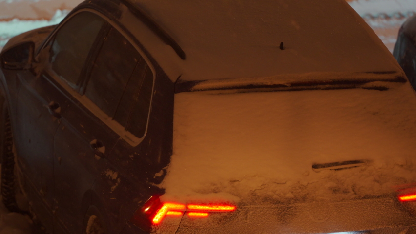 Parked cars covered with snow at dusk under a street lamp in parking lot in winter. Heavy snowfall on city streets. High quality 4k footage