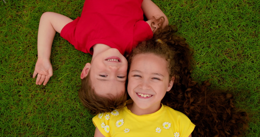 Happy little brother and sister lies on green grass. Children is dream on the grass in park. Happy face of baby. Little boy and girl looks at sky. Smile of Children and look up to camera