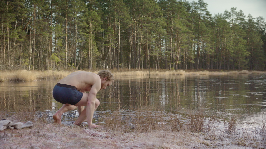 WIDE SHOT - An ice bather slips into the ice hole he has made in the frozen lake
