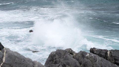 Foamy Sea Waves Crashing On Rocks At The Shore In Genoa, Italy. panning left, slow motion