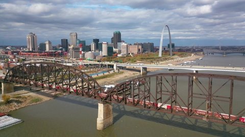 ST. LOUIS MISSOURI - CIRCA 2020s - Aerial of a freight train crossing the Mississippi River with the St. Louis Gateway Arch.