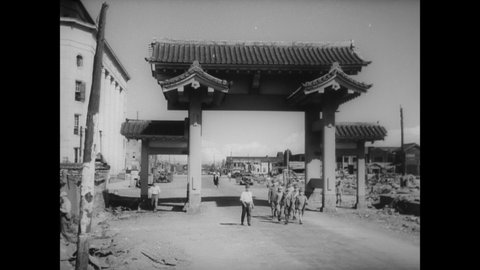 CIRCA 1945 - Japanese soldiers march under an arch in a war-torn city.