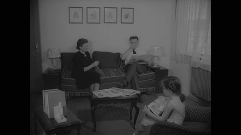 CIRCA 1937 - Members of a small family read in their New York living room, and interiors of the other rooms in the house are spacious and clean.