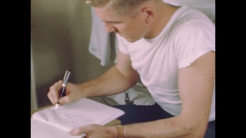 CIRCA 1944 - An American soldier writes a letter home while on a troop transport ship, where other men are resting or playing cards.