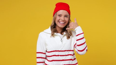 Beautiful vivid young girl teen student wears striped white shirt hat point finger camera on you doing phone gesture like says call me back blinking isolated on plain yellow background studio portrait