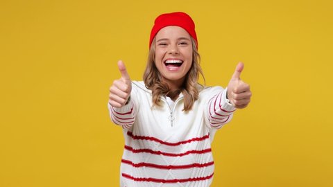 Excited cheerful blithesome young girl teen student wears striped white shirt hat showing thumb up like gesture isolated on plain yellow background studio portrait. People emotions lifestyle concept