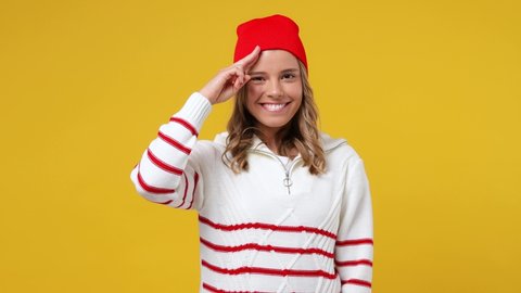 Beautiful cheery happy fun young girl teen student wears striped white shirt hat looking camera saluting greeting isolated on plain yellow background studio portrait. People emotions lifestyle concept