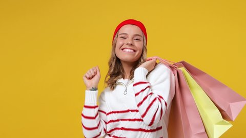 Excited young girl teen student wears striped shirt hat hold package bags with purchases point on workspace area copy space mock up wave hand come isolated on plain yellow background studio portrait