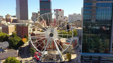 ATLANTA, GEORGIA - CIRCA 2020s - Aerial of ferris wheel reveals Olympic Park in downtown Atlanta, Georgia and city skyline.