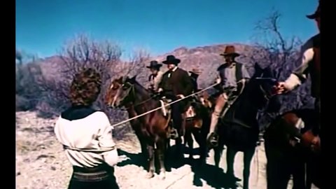 CIRCA 1974 - In this western film, an outlaw on horseback drags a minister behind him on the desert floor.