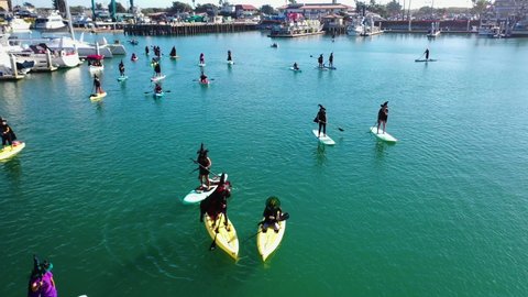 VENTURA, CALIFORNIA - CIRCA 2020s - Aerial witches paddle on surfboards and paddleboards to celebrate Halloween in Ventura harbor, California.