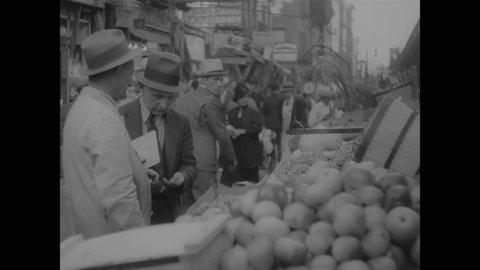 CIRCA 1937 - People shop at an open marketplace on New York's Delancey Street.