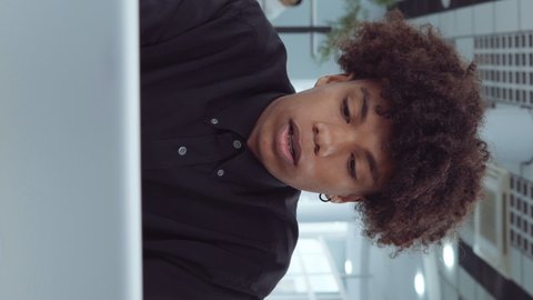 Vertical Screen: African American employee using laptop in office and mumbling something, diverse coworkers on background. Arc shot man working online, browsing internet. Concept of business