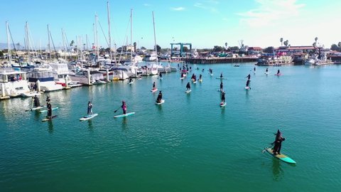 VENTURA, CALIFORNIA - CIRCA 2020s - Aerial witches paddle on surfboards and paddleboards to celebrate Halloween in Ventura harbor, California.