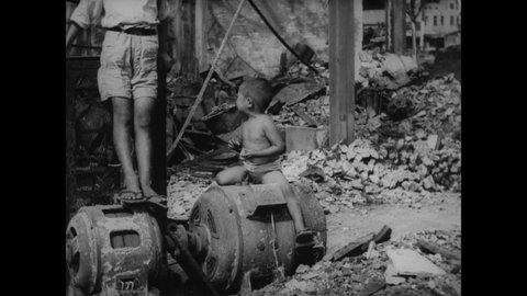 CIRCA 1945 - A crying little Japanese boy sits amidst rubble in his war-torn neighborhood.