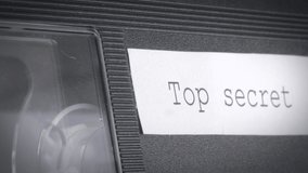 Closeup shot of a working vhs cassette with a top secret sign on it. Camera slowly zooming out.