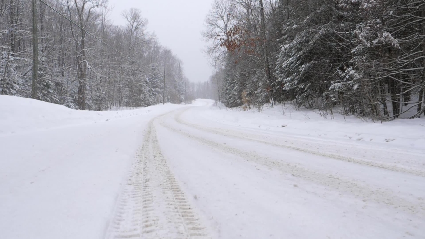Tire tracks on curvy rural snow-covered winter road. Slow motion snow falling. Haliburton, Ontario, Canada. Royalty-Free Stock Footage #1083655915
