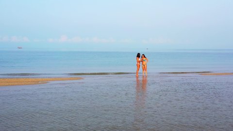 Two tourist girls taking photos on exotic beach with calm sea background and cloudy sky background in Ko Pha Ngan in Thailand