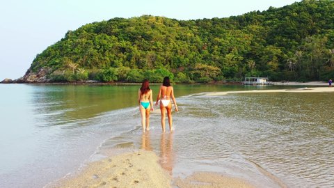 Young women in swimsuit washing their feet on crystal water of shallow lagoon on exotic beach of tropical island called Ko Pha Ngan in Thailand