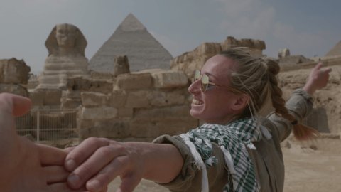 Slow motion: Follow me concept: Young woman holding companion hand, leading him towards the Great Pyramids of Giza. People travelling adventure concept. 