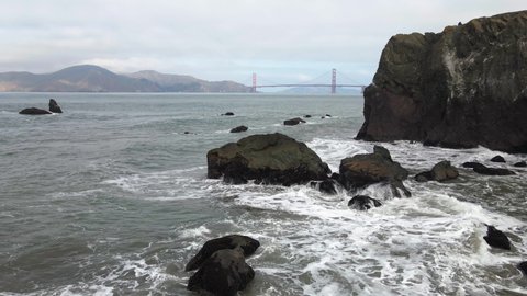 Aerial drone view over rocks and waves the Golden gate bridge in the background