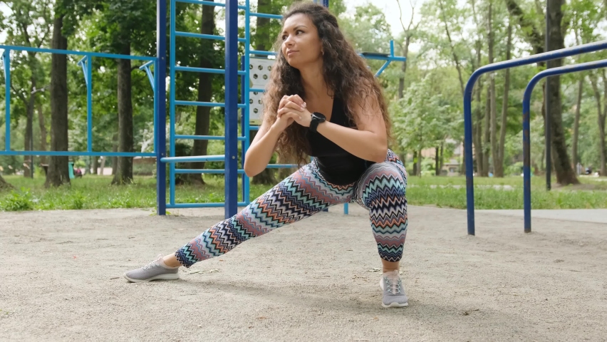 Pretty girl doing stretching side squats outdoors. Young woman exercising outside and make buttoms workout
