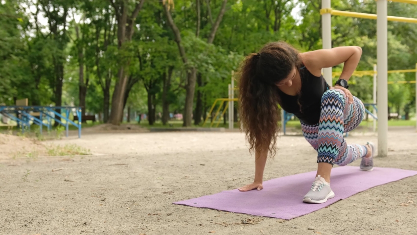Pretty girl doing stretching side squats outdoors. Young woman exercising outside and make buttoms workout