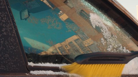 Clearing snow and ice from a car window before driving to work is a problem for motorists in countries with cold climates. Close-up of a brush is held on the glass, clearing snow from the window.