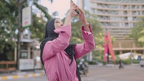 Asian Muslim girl wear hijab using smartphone taking pictures of city view, sightseeing tourist, modern technology connecting people sending photo messages, internet access, phone camera resolution