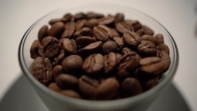 A glass of roasted coffee beans rotates on the table. Close-up shot. Coffee as a tonic drink. The harm of drinking coffee.