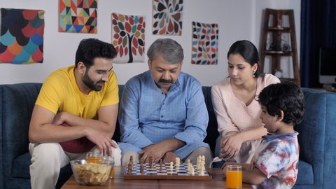 An aged man with grey hair and his young son playing a game of chess together. Family members of different generations sitting together in the living room - leisure time, family bonding, large family
